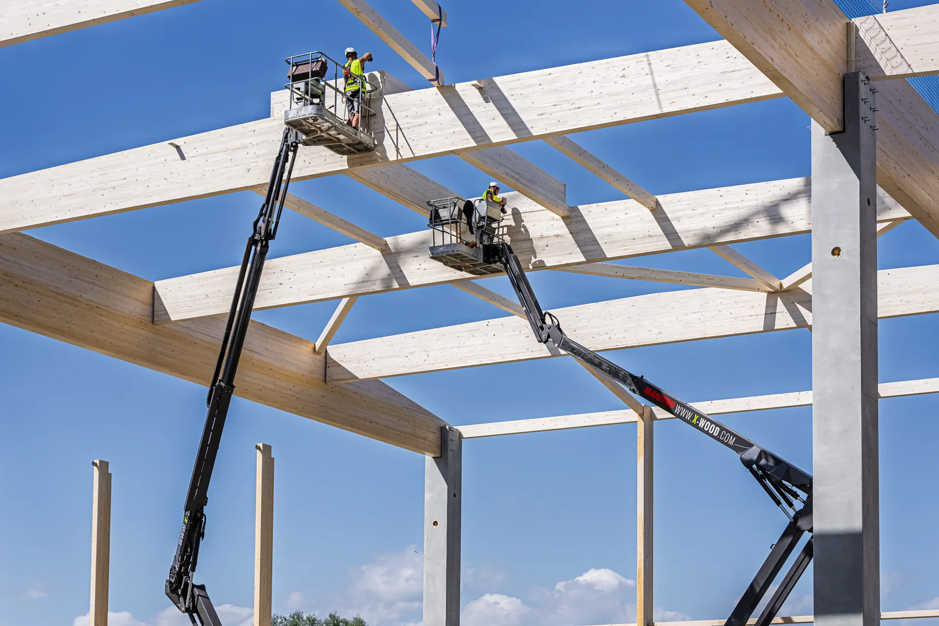 Two X-Wood® fitters placing the roof beams of a timber hall from cherry pickers