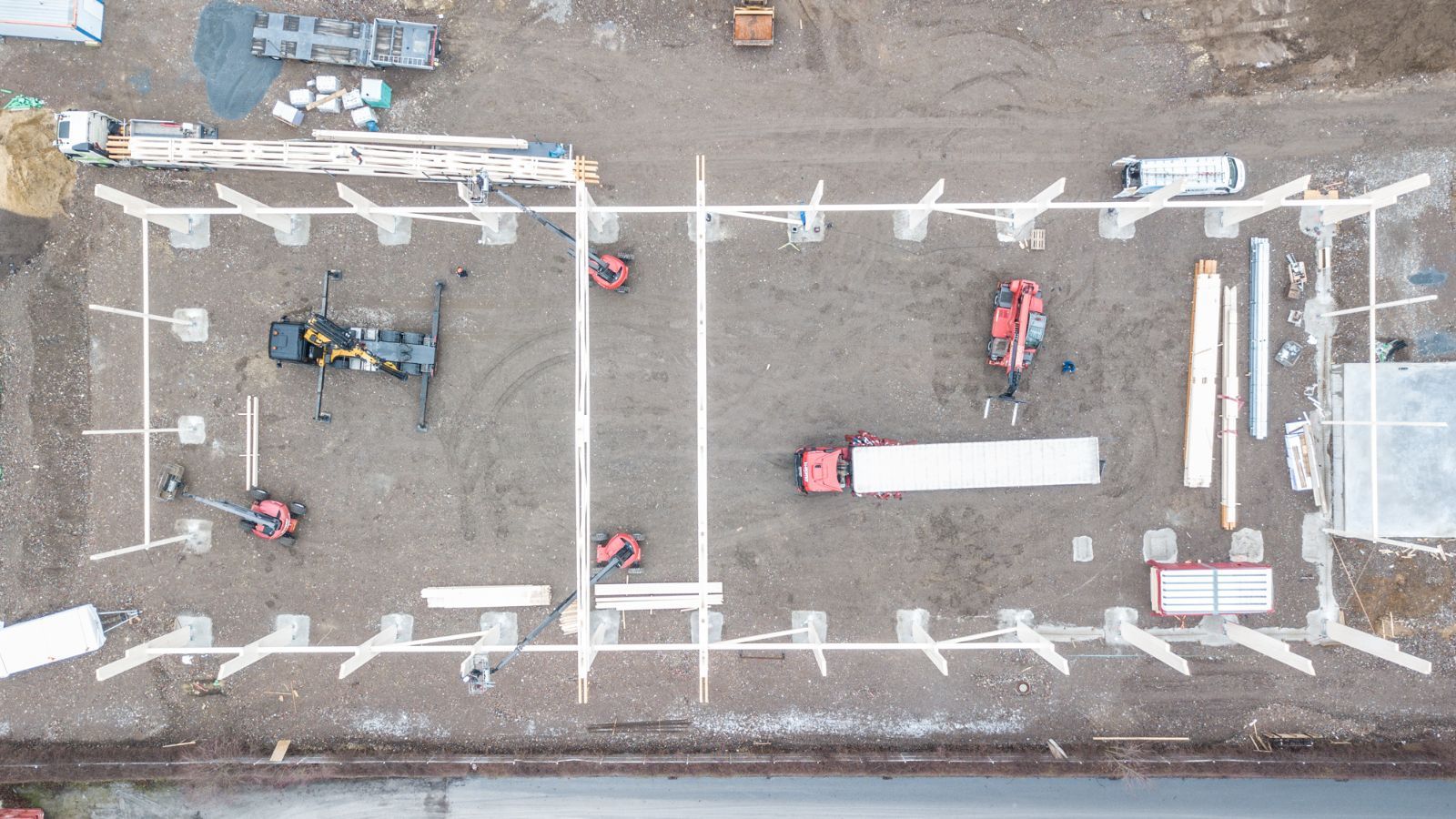 Drohnenaufnahme einer Hallenbaustelle mit gestellten Fundamentstützen und Montagefahrzeugen